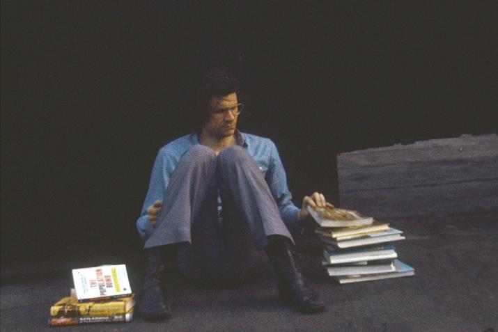 person sitting on the ground on a rooftop with a large pile of books beside them