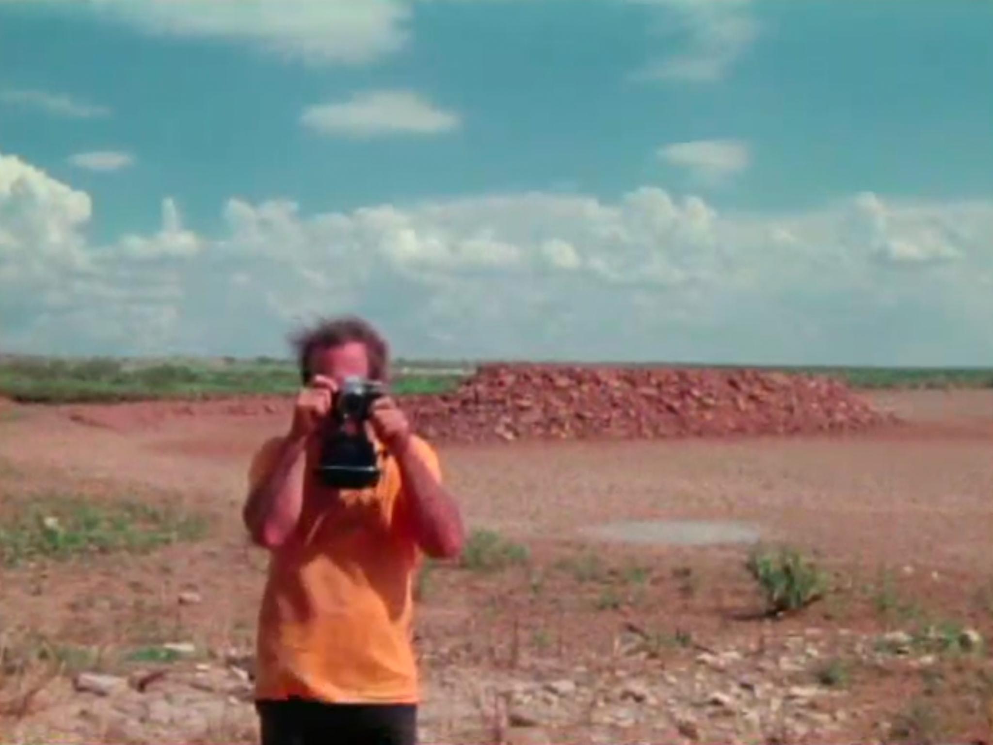 A young man taking a picture toward the camera with a dry lakebed in the background.