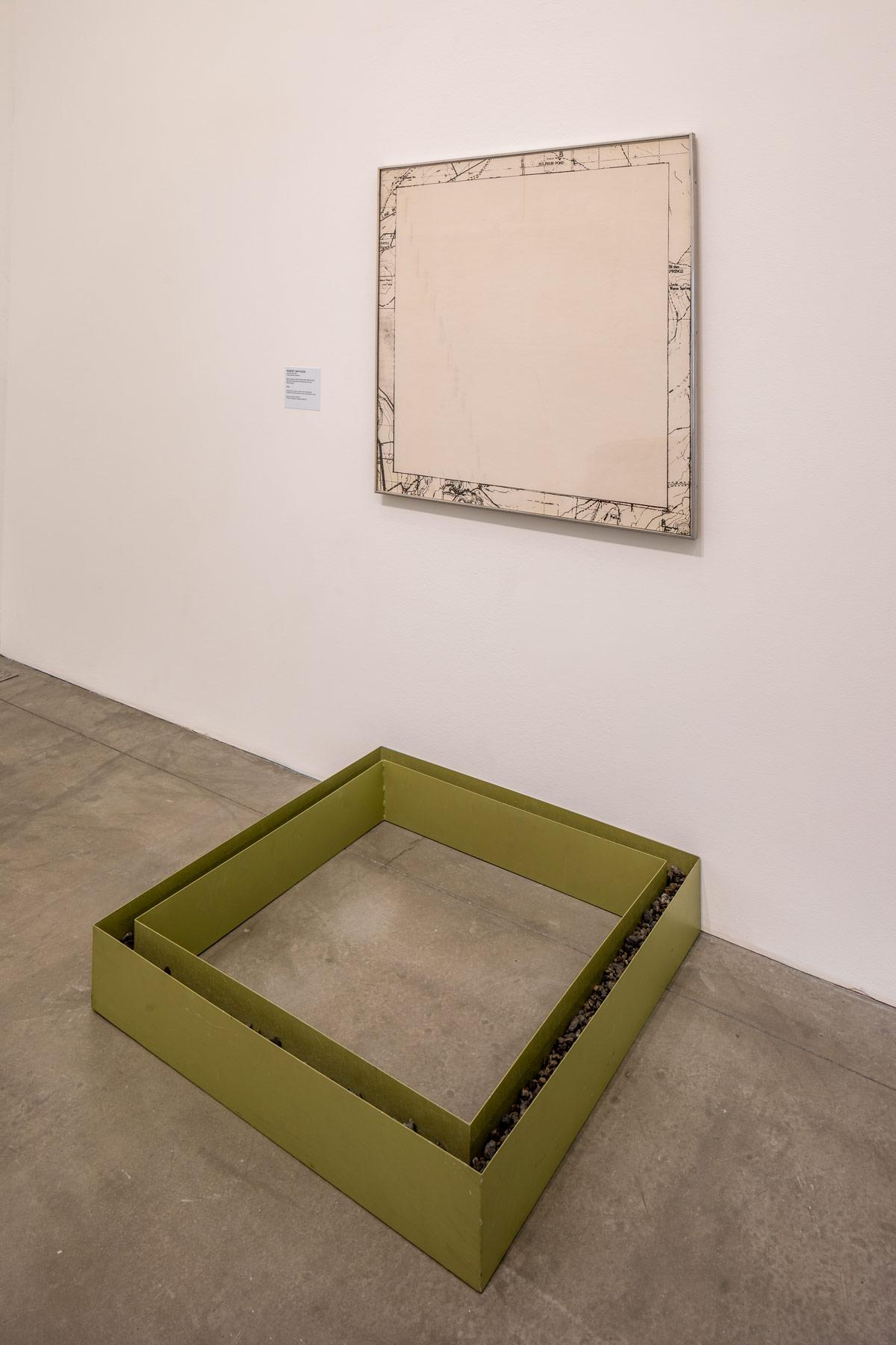 wall and floor with a square map on the wall and a square metal box of the same shape and size on the floor