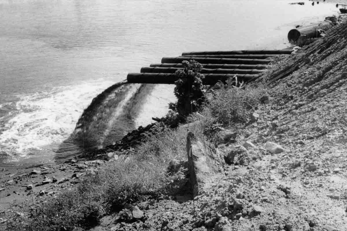 black and white image of pipes gushing water into a river