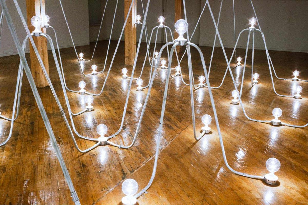 a sculpture made of arches of conduit with lightbulbs on the floor and at the peaks of the arches