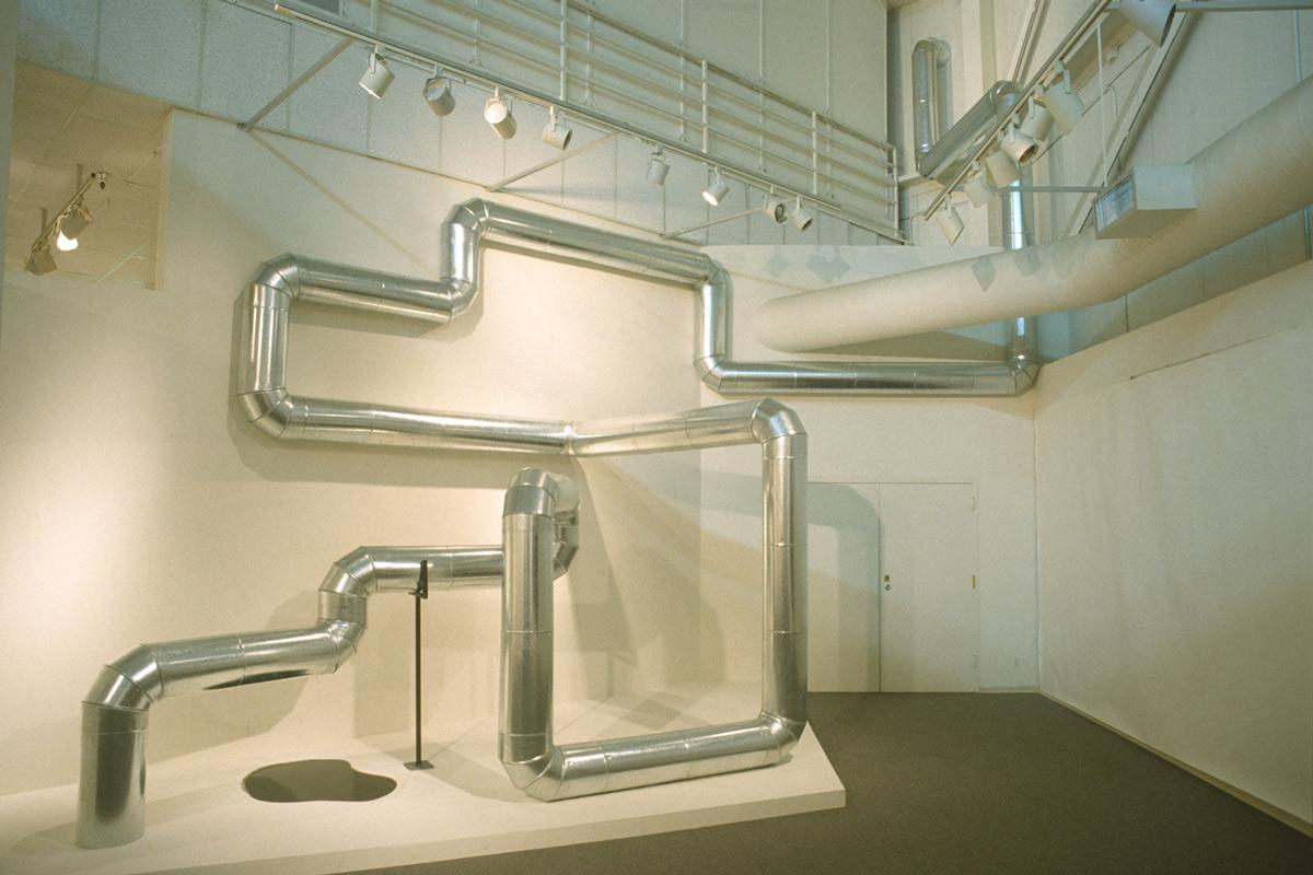 steel duct zig zags through the air and along walls in a white gallery space