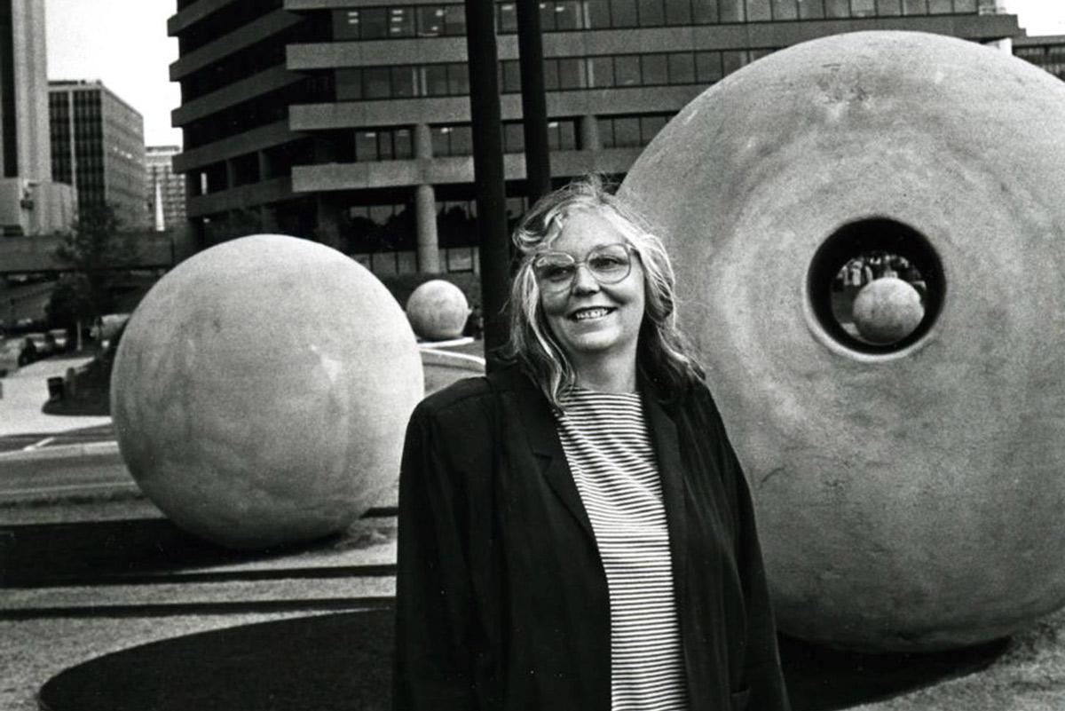 figure standing a city park with large concrete spheres behind