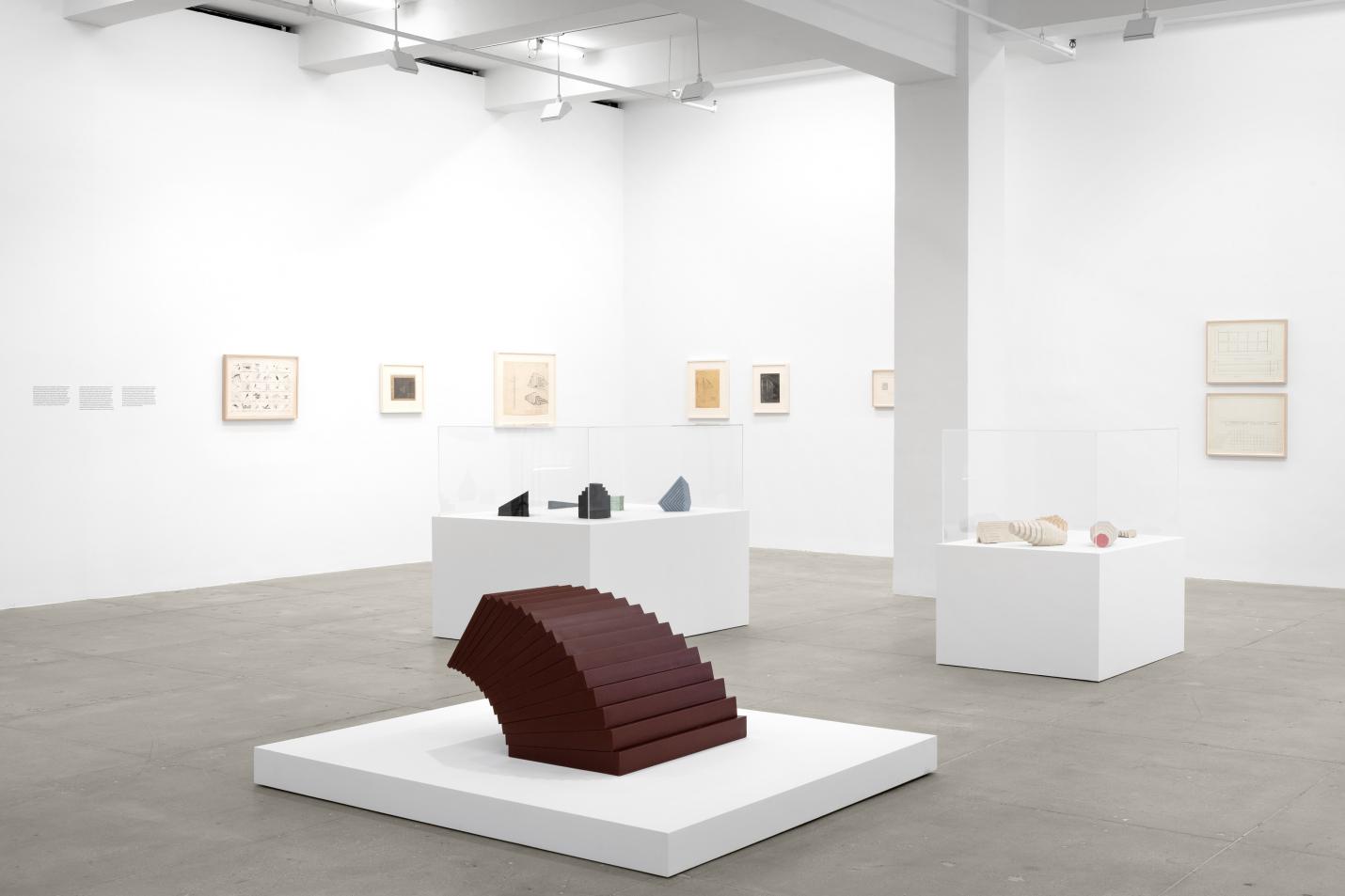 a gallery filled with sculptures on white plinths and drawings hung on the walls