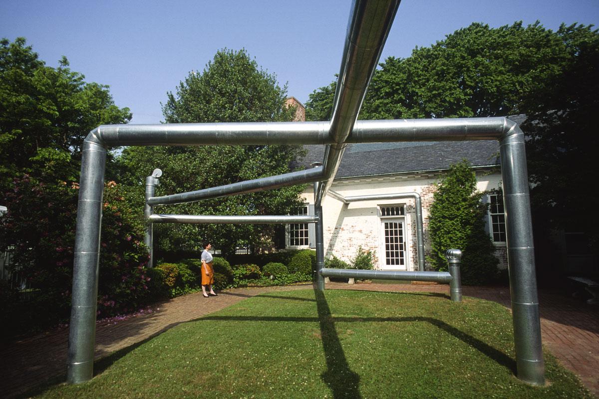 large steel duct coming out of the ground and spanning large gaps with a person standing underneath