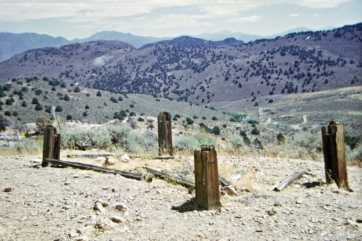 four wooden pillars sticking out of the earth with mountains in the background