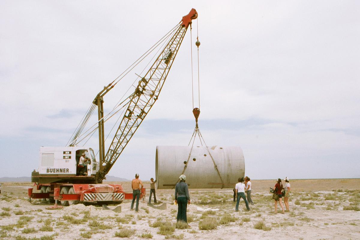 a large crane lifting one of Nancy Holt's Sun Tunnels into place with people surrounding