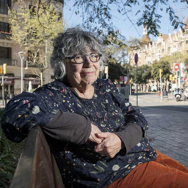 Woman with gray hair and glasses sitting on a bench looking at the camera.