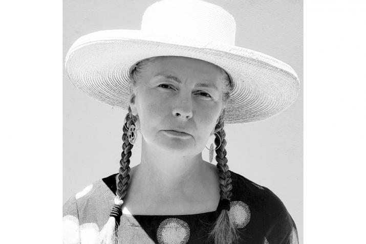 black and white image of a woman looking at the camera with braids wearing a white hat