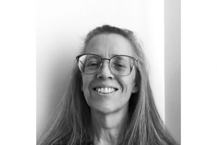 black and white image of a person smiling at the camera with long hair and glasses