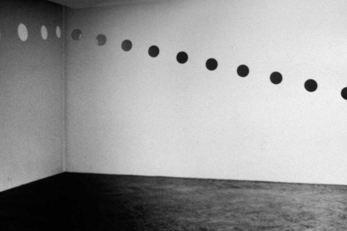 a corner of a room where circular mirrors are hung in a diagonal line on one wall, and circle orbs of light are reflected onto the other wall