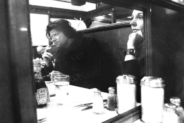 two people site at a diner table looking forward, one smokes a cigarette. black and white.