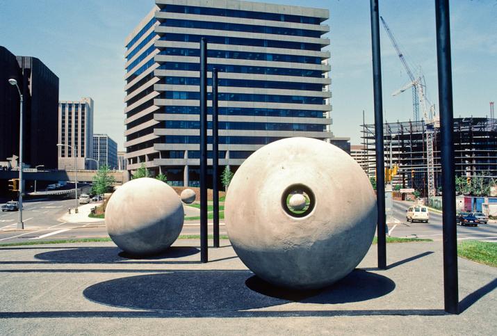 two large concrete spheres surrounded by steel poles and shadow markings on the ground in an urban environment