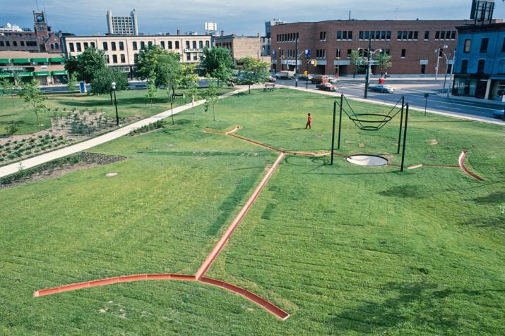 a city park with green grass and red tile channels cut into the lawn with a large metal structure over a large drain