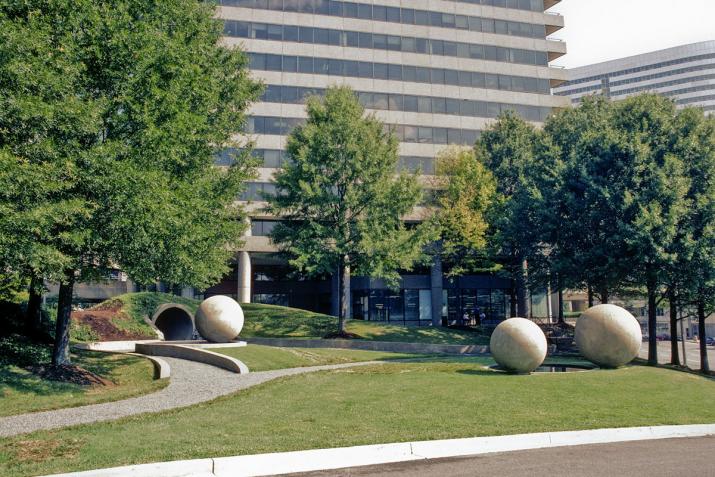 three large concrete spheres and one circular tunnel surrounded by trees, grass, and large buildings