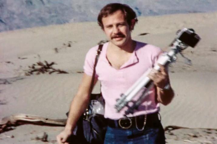 a man standing in the desert holding a tripod and camera gear
