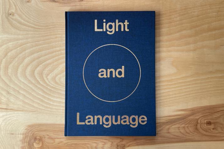 a blue book that says "Light and Language" resting on a plywood table