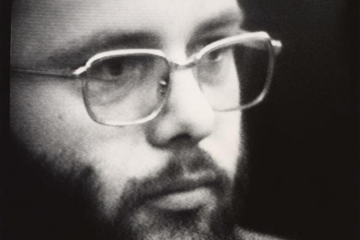 Black and white image of a man with a beard and glasses talking looking to the left.