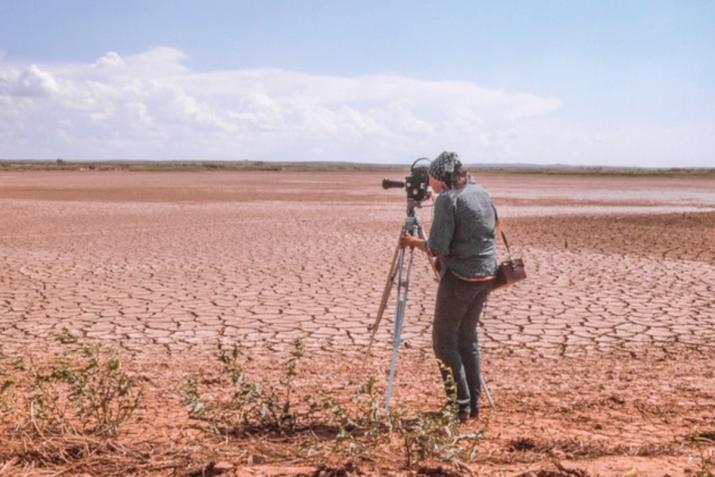 A person looking through a film camera on a tripod, overlooking a dry lakebed.