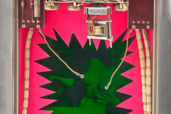 a wall sculpture with bright neon colors and machine parts interacting with a cutout image of a woman