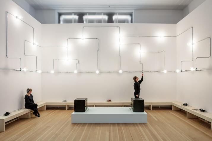 A network of conduit a lightbulbs on three walls above two people sitting 