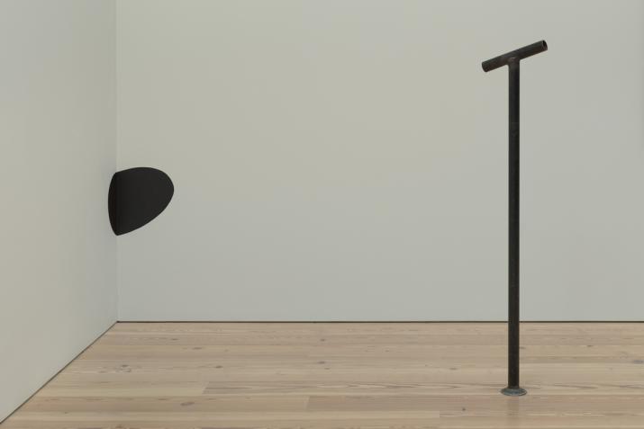 A black metal pipe with a horizontal top is pointing directly at a black circle painted on the wall