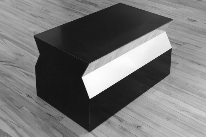 a trapezoidal low sculpture made of formica and mirrors on a wood floor