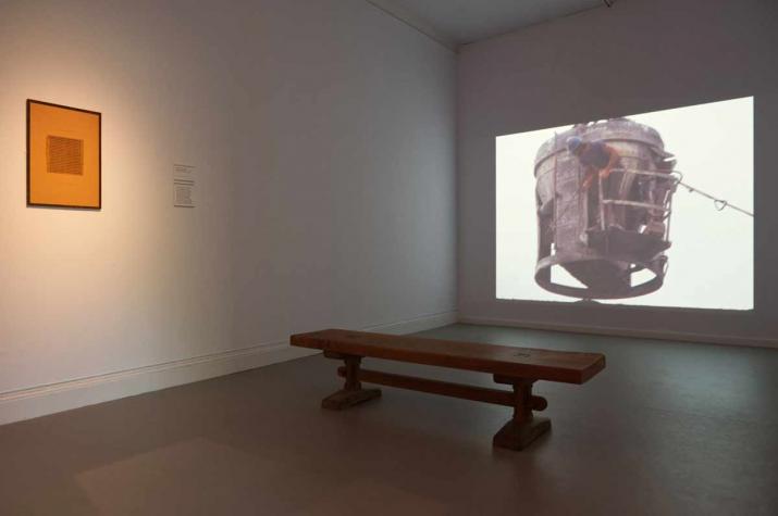 a gallery with a projection of a film on the right and a small framed work on the wall on the left