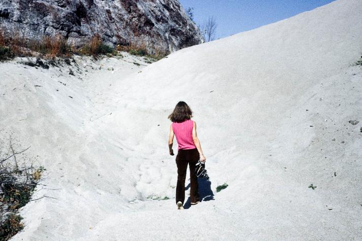 a woman walking up a sand dune hill with her back to the camera