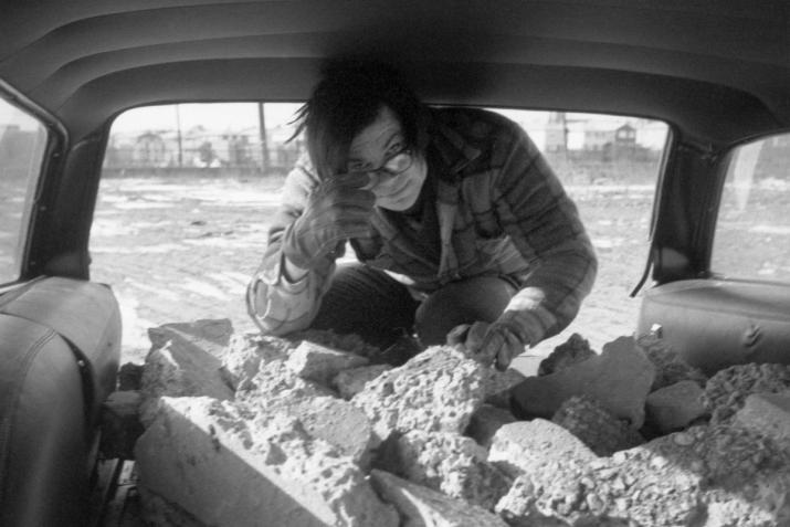 Robert Smithson looking at the camera from the back of a stationwagon loaded with rocks