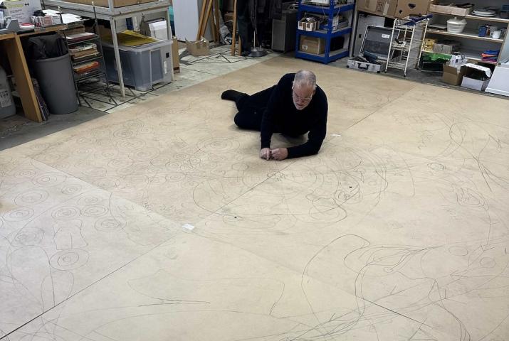 an artist working on a large drawing on the floor of their studio