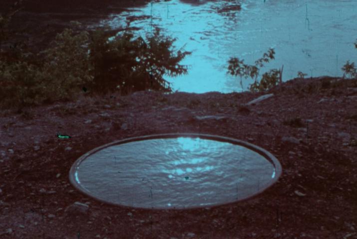 film still of a circle of water beside a river