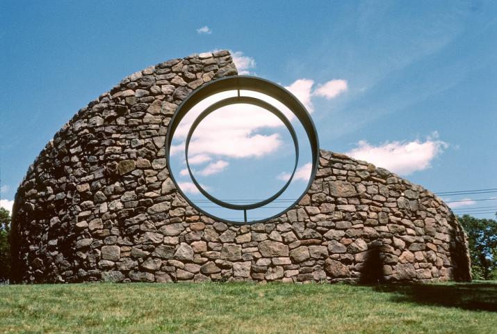 a sculpture made of a curved stone wall with a viewing circle within it