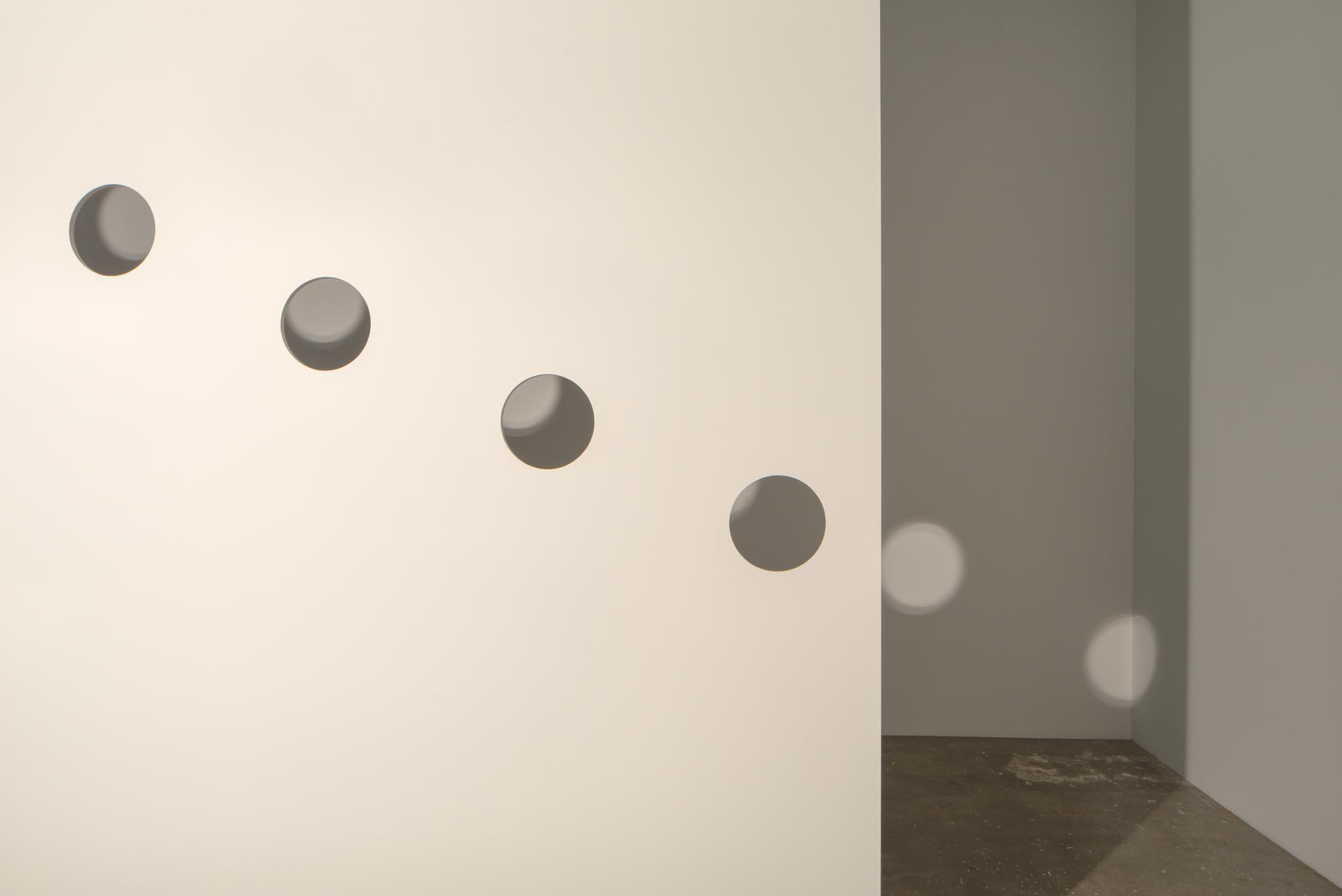 Light hitting a wall in the middle of a room, with holes cut in the wall to allow circles of light to be cast on the back wall.