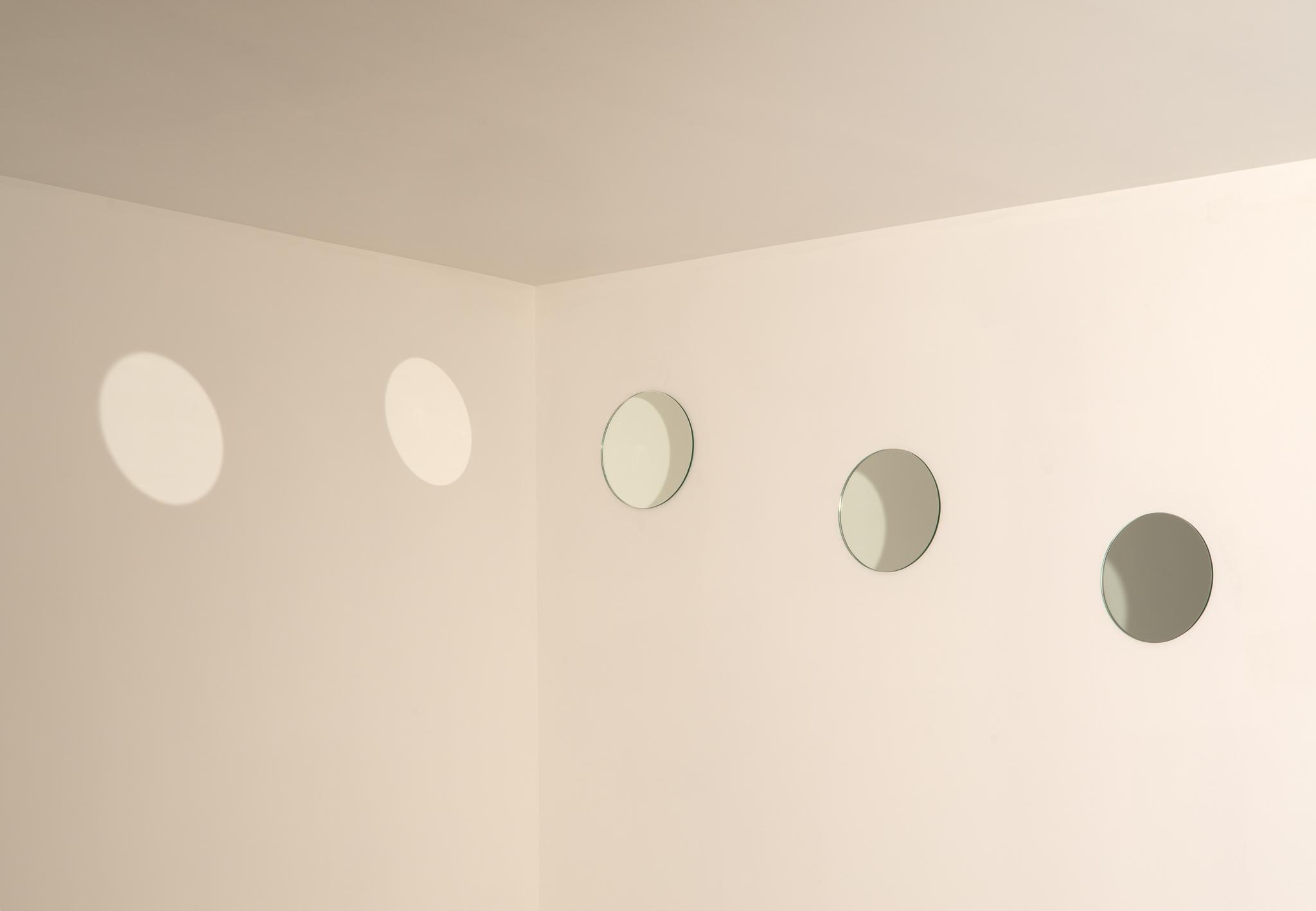 Two white walls meeting a white ceiling with three small round mirrors on the right side and reflected circular light on the left side.