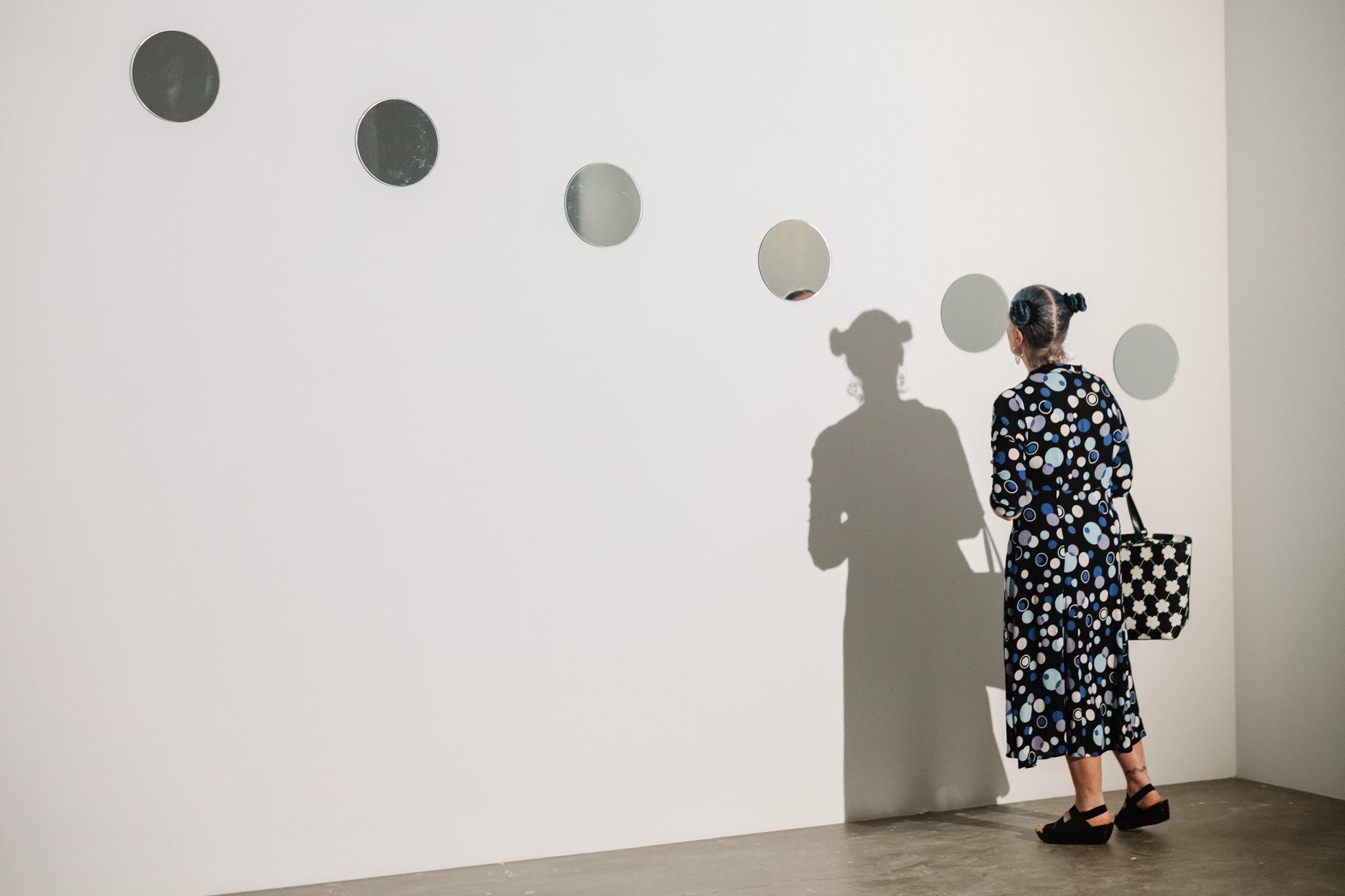 Woman looking at small circular mirrors on wall as part of Mirrors of Light I.