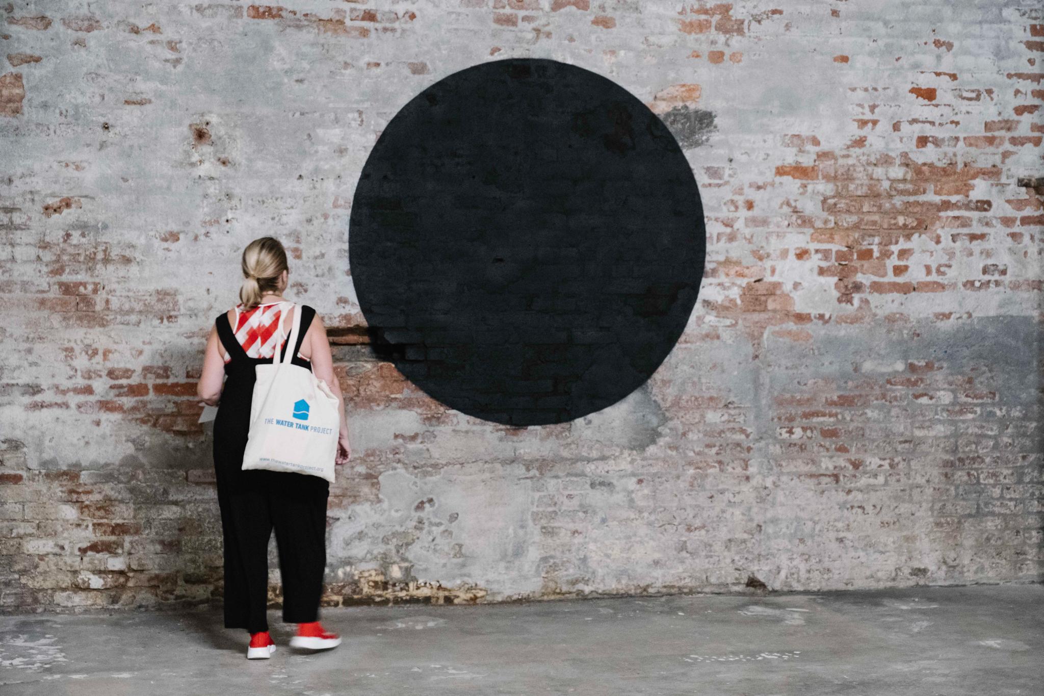 Woman looking at black circle painted on brick wall as part of Dual Locators.