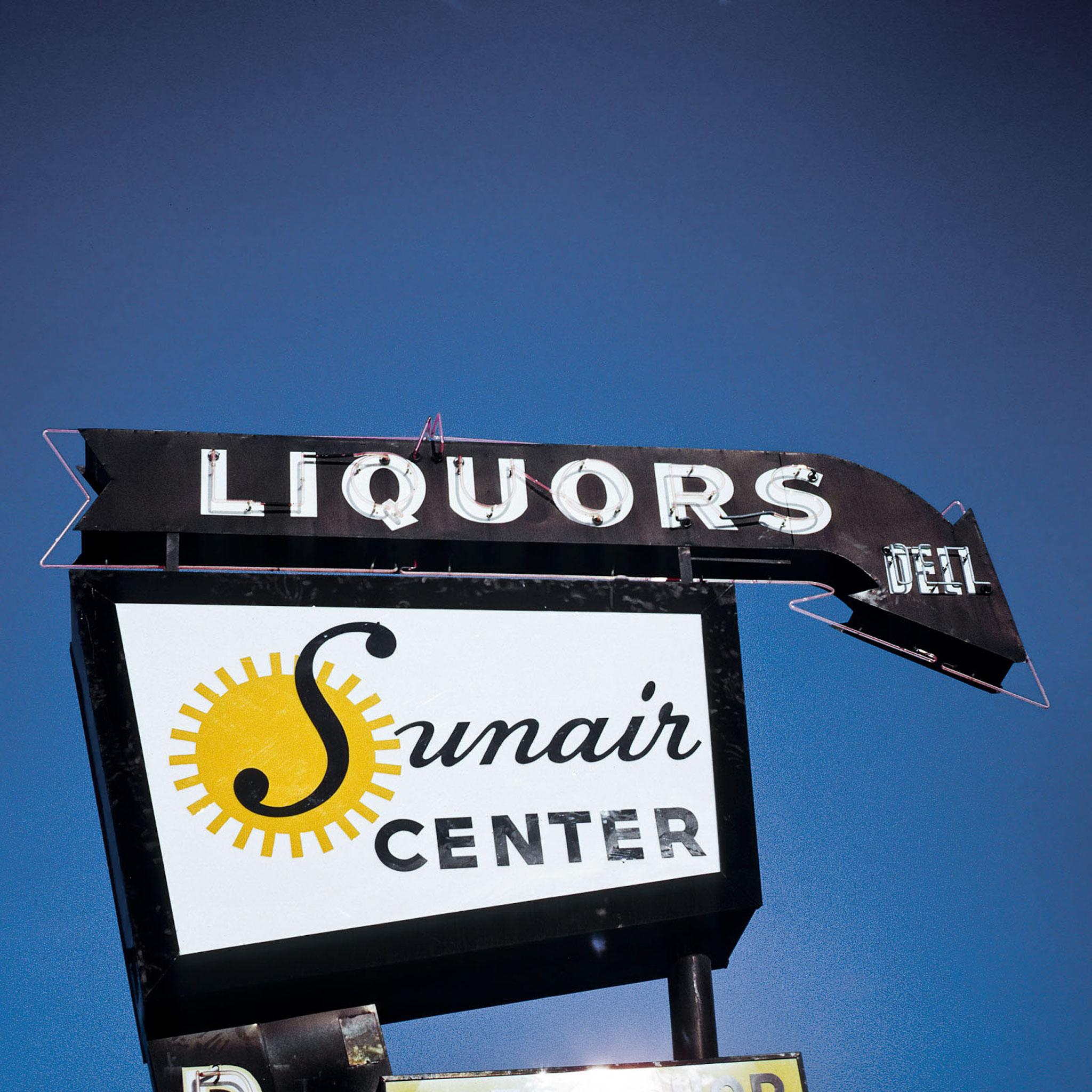 A sign against a blue sky that says "Sunair Center" and "Liquors, Deli"