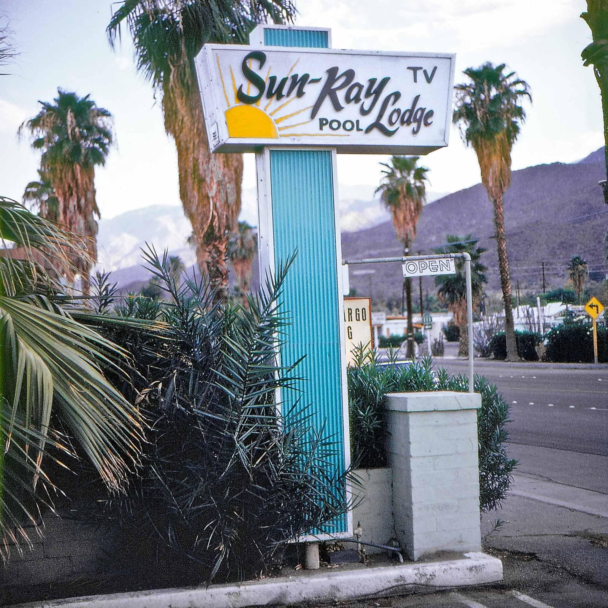 A sign that says "Sun-Ray Lodge" with Palm trees in the background