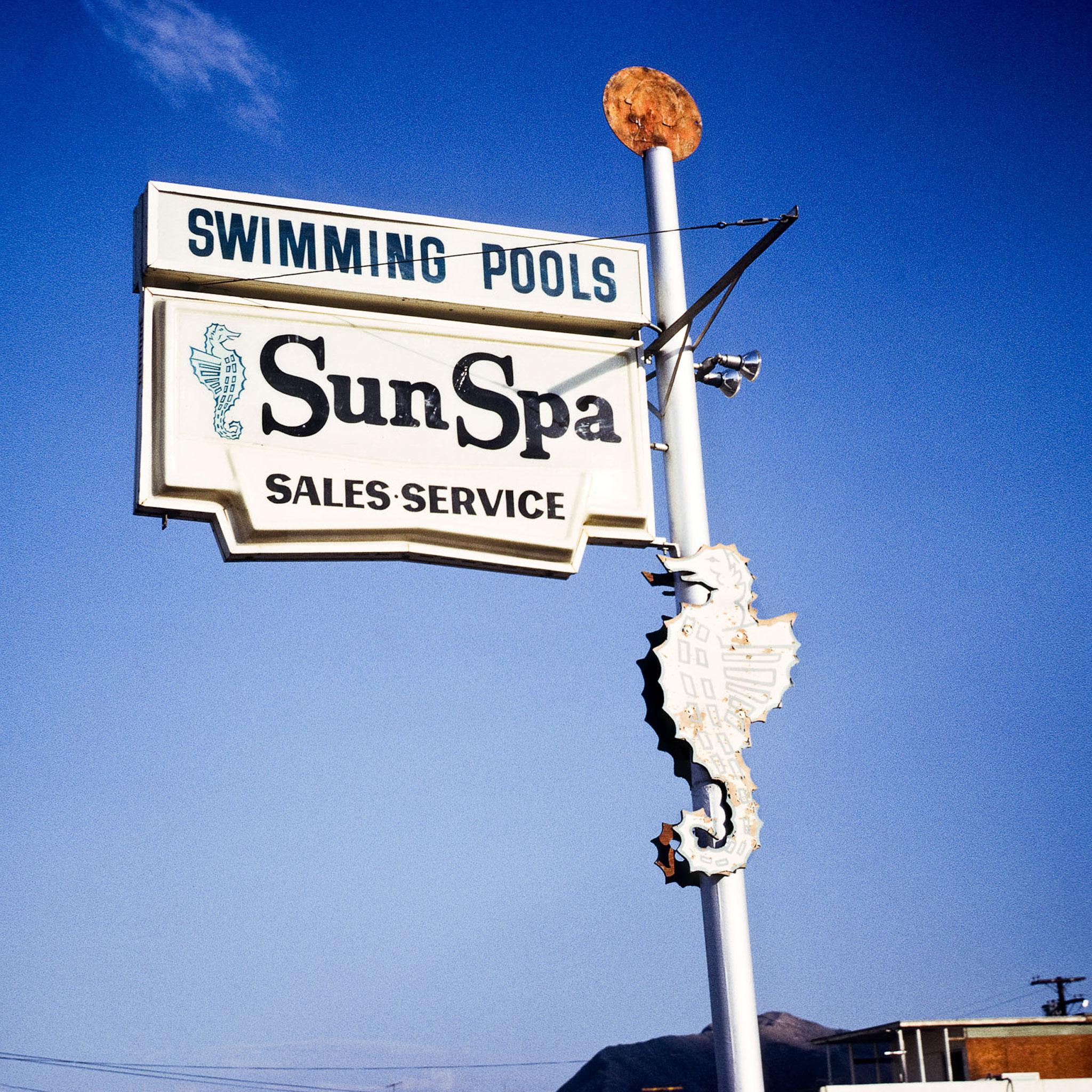 A sign that says "SunSpa, Sales Servies" and "Swimming Pools" against a blue sky