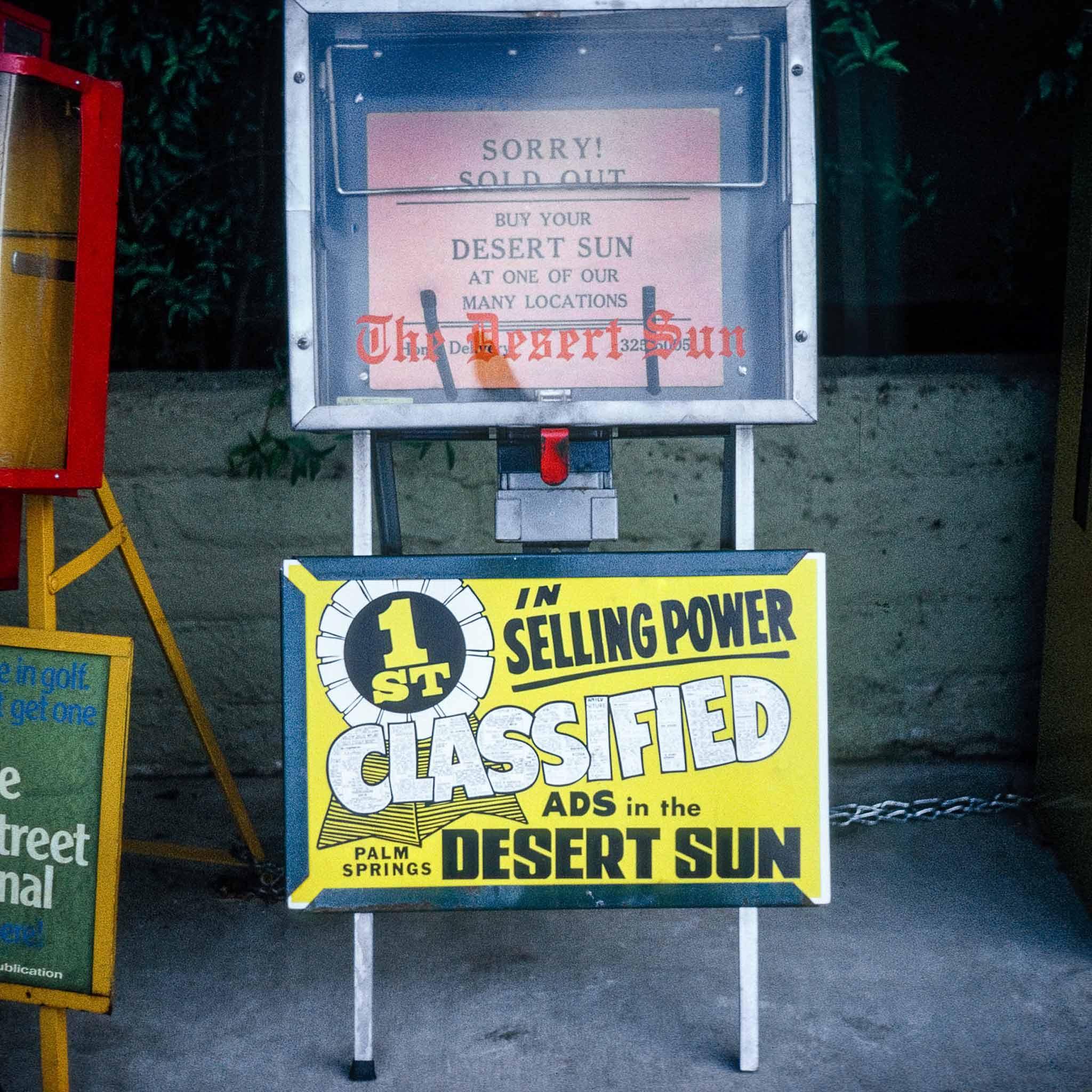 A sign in front of a newspaper box that says "1st in Selling Power Classified Ads in the Desert Sun"