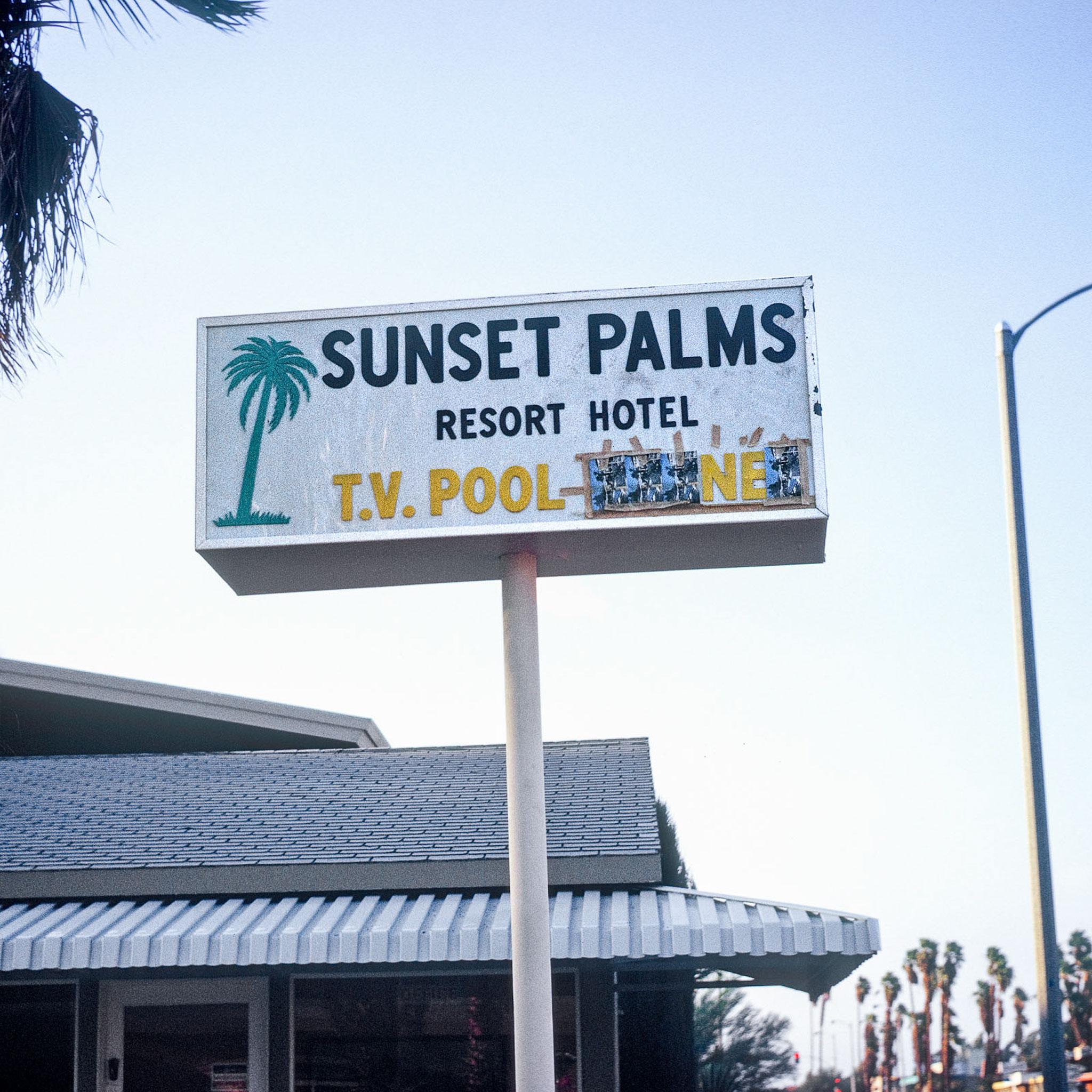 A sign that says "Sunset Palms Resort Hotel T.V. Pool" against a blue sky