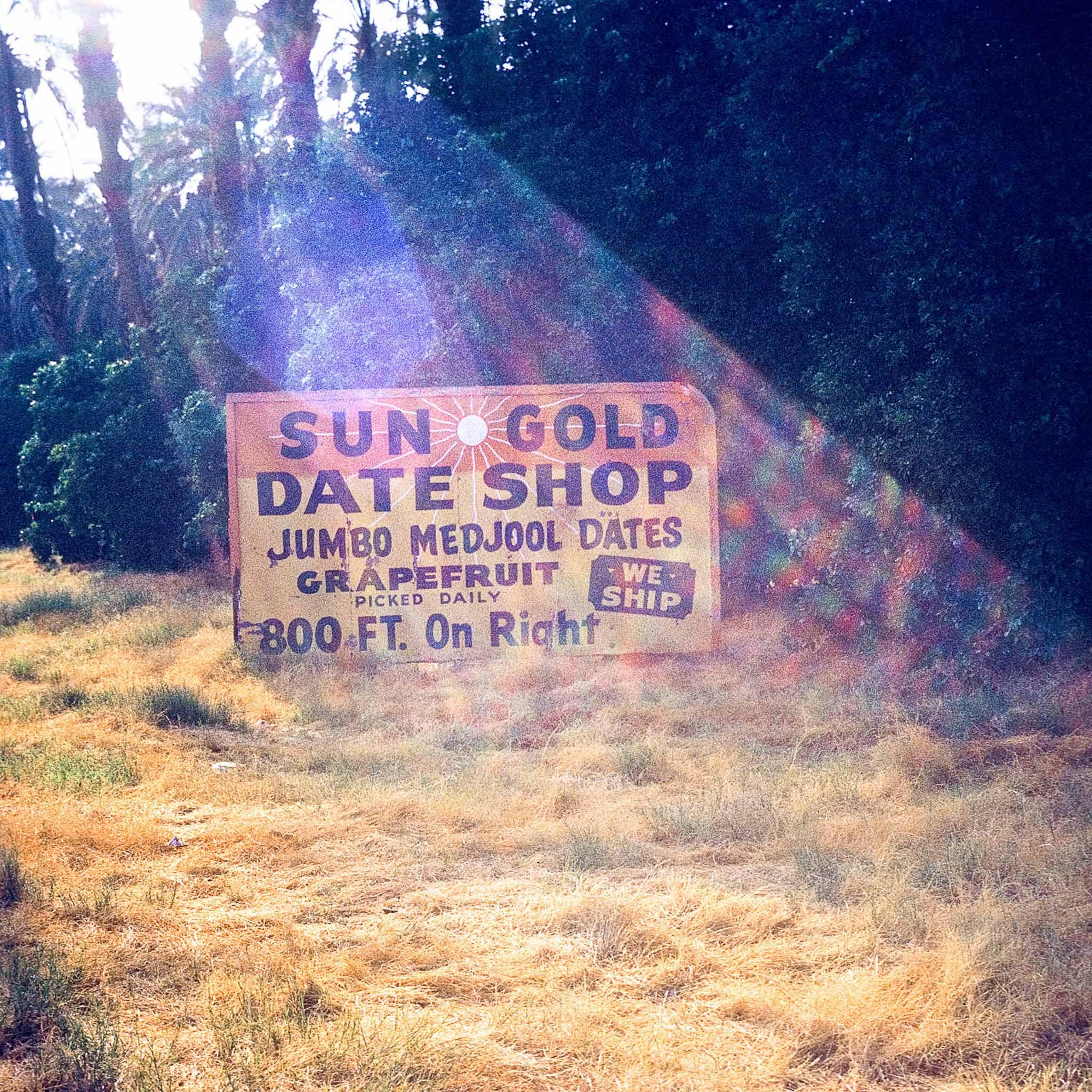 A sign in a meadow that says "sun Gold Date Shop"