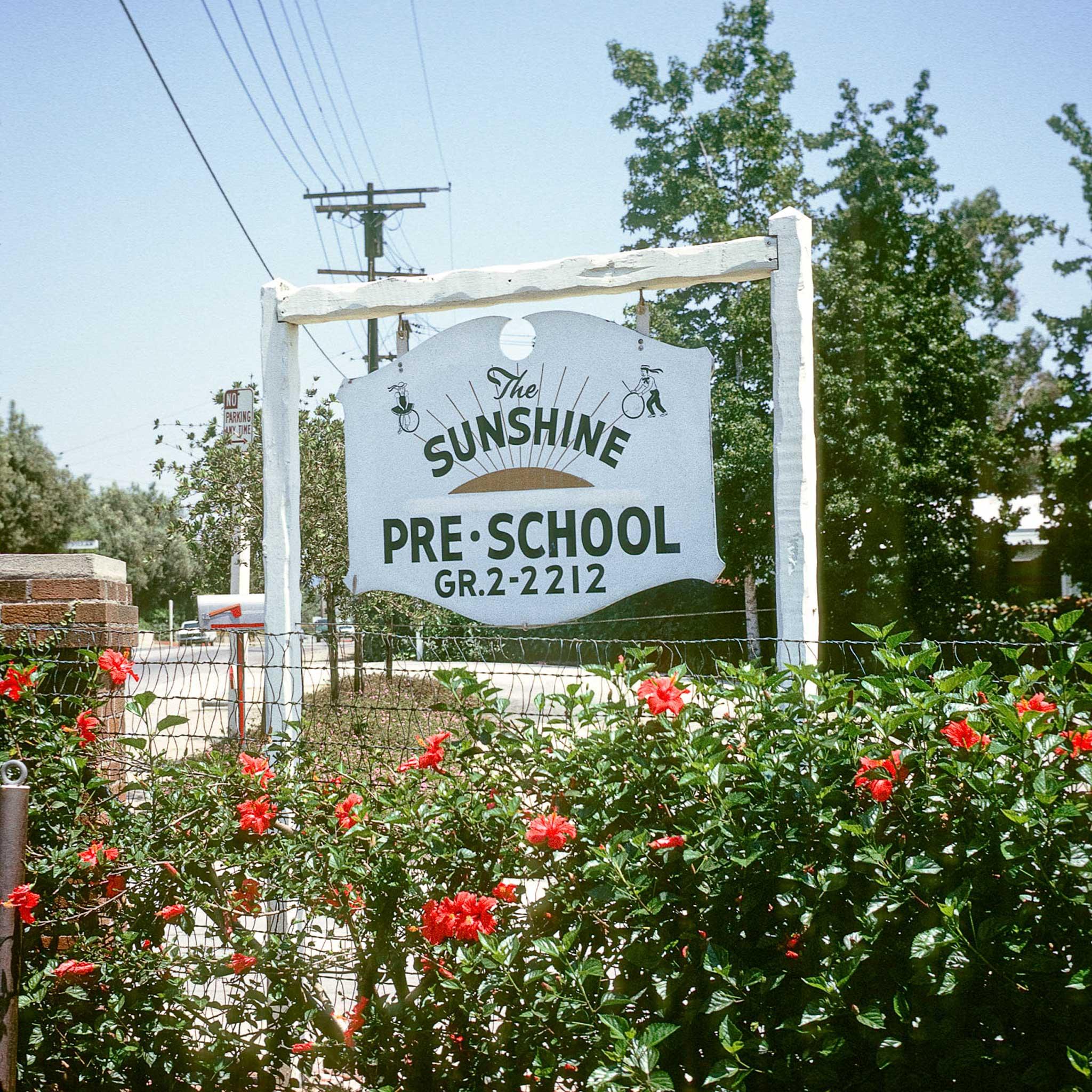 A sign that says "The Sunshine Pre-School" above a rose bush