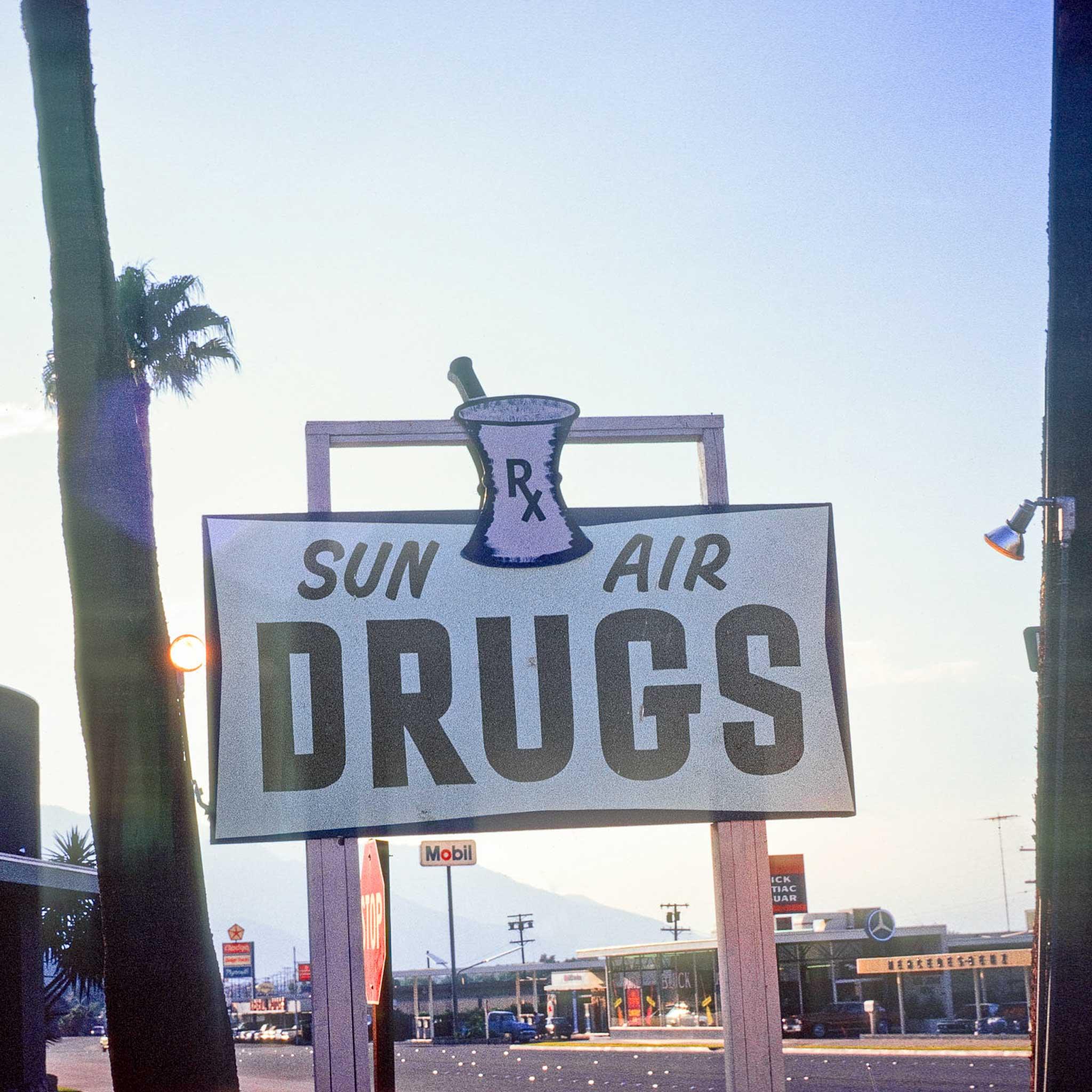 A sign that says "Sun Air Drugs" with a blue sky and palm trees in the background