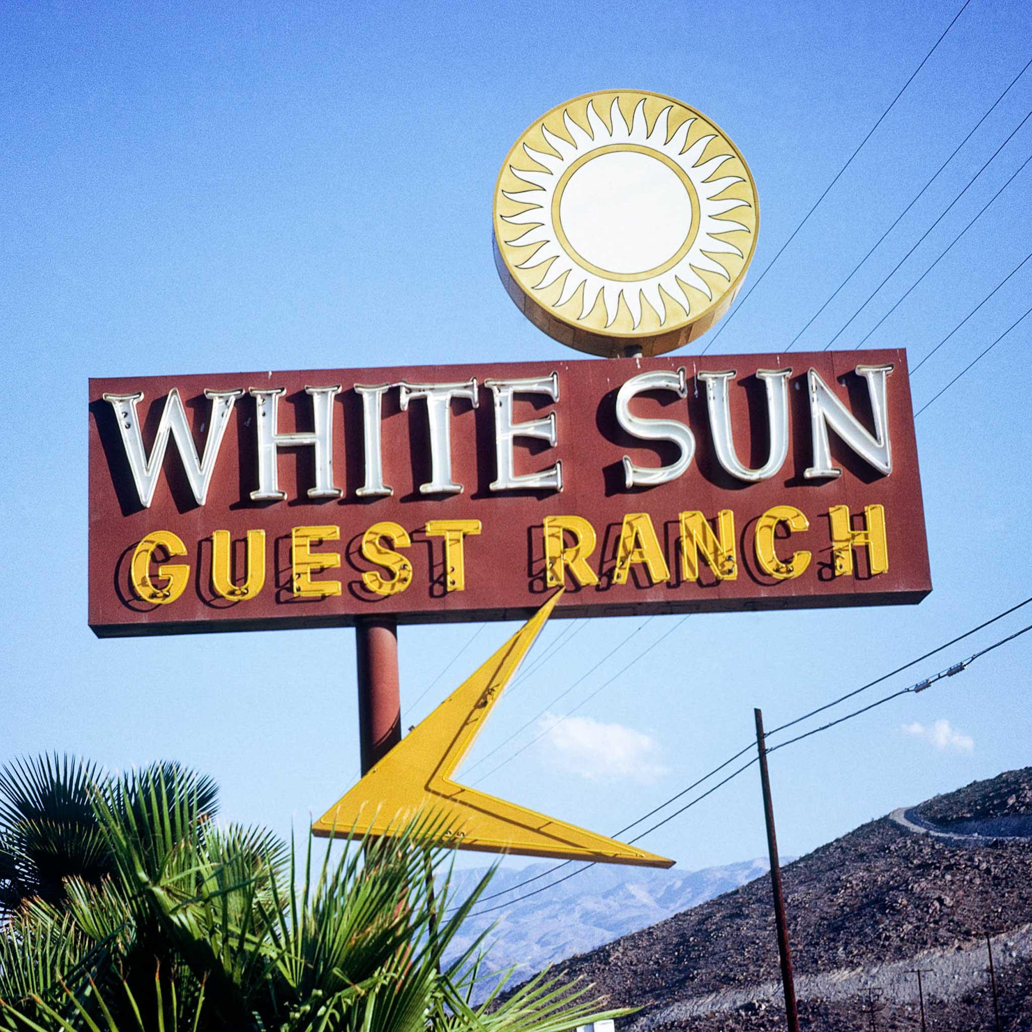 A sign that says "White sun guest ranch" with a yellow and white sun graphic