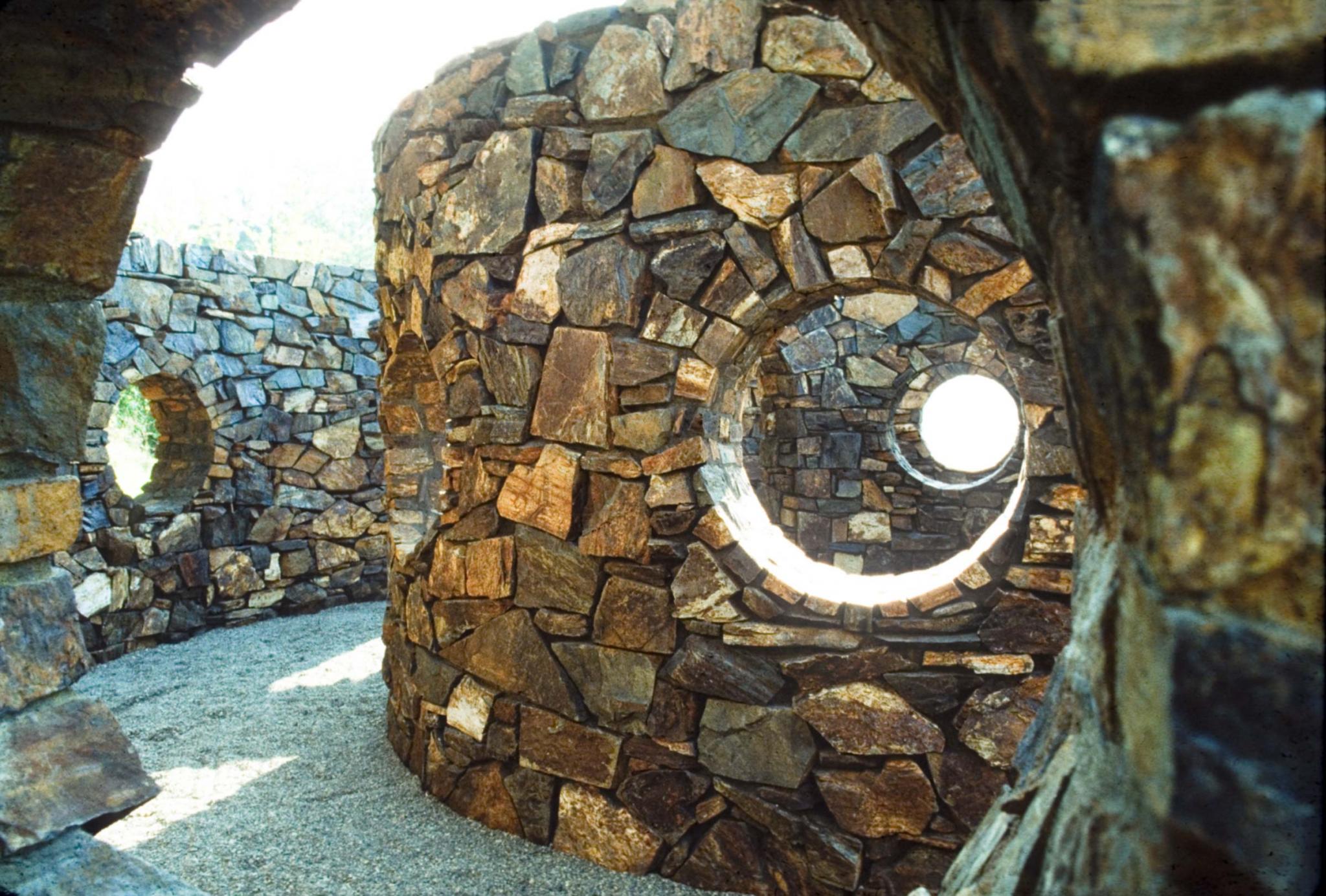 Looking through a circular opening at another curved stone wall with another circular opening in it.