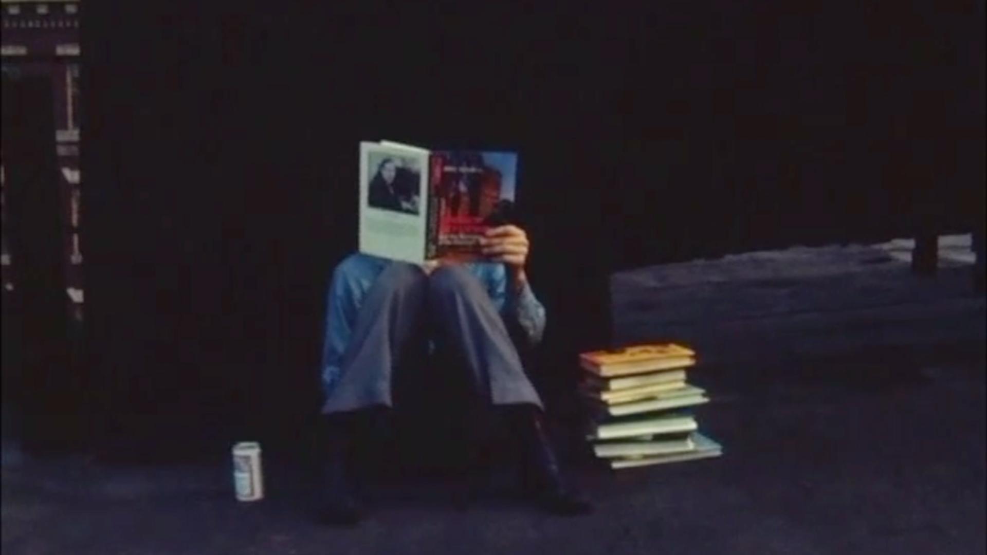 man sitting on the ground reading a book with a pile of books next to him