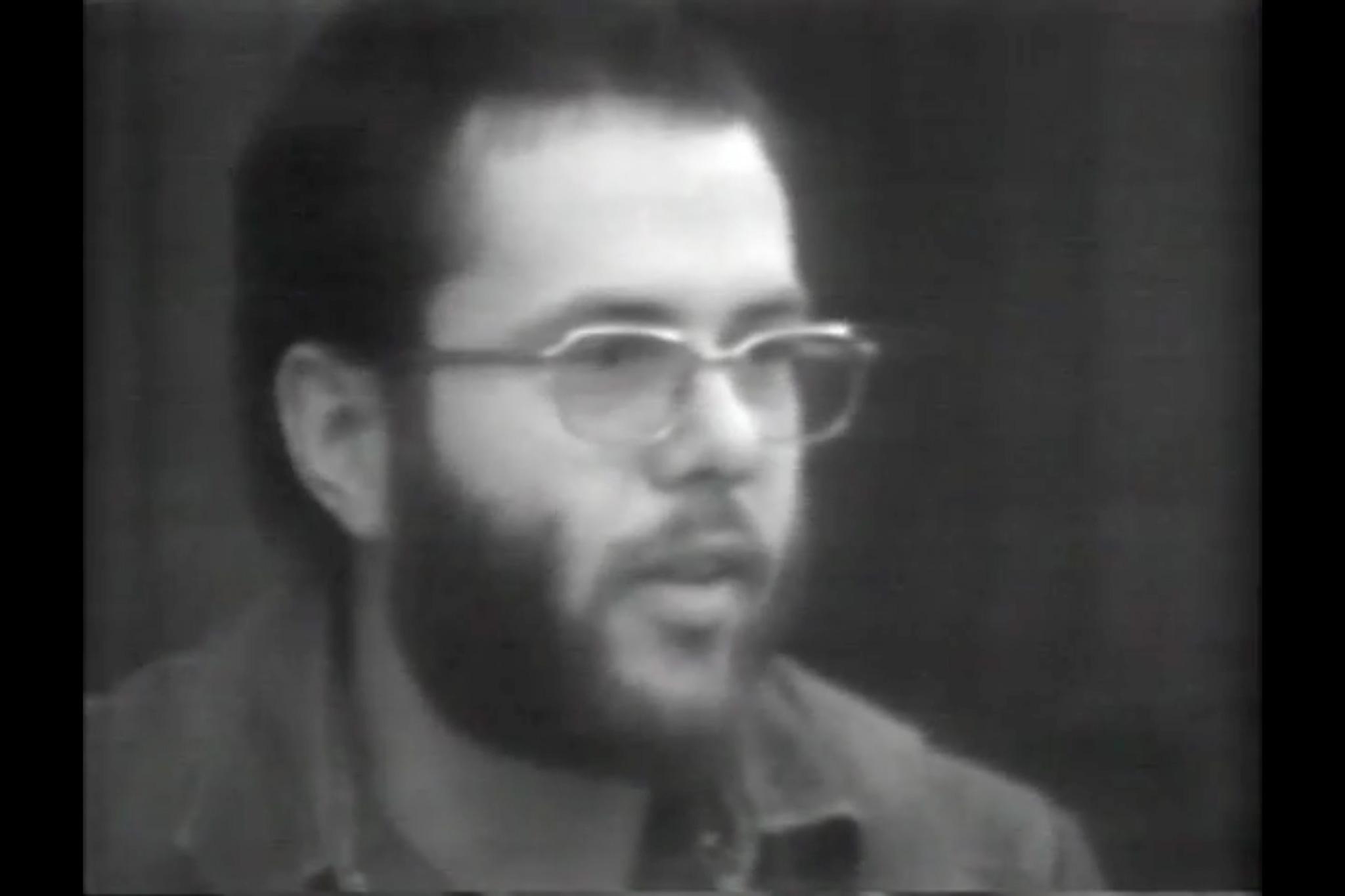 Black and white image of a man with a beard and glasses talking looking to the right.