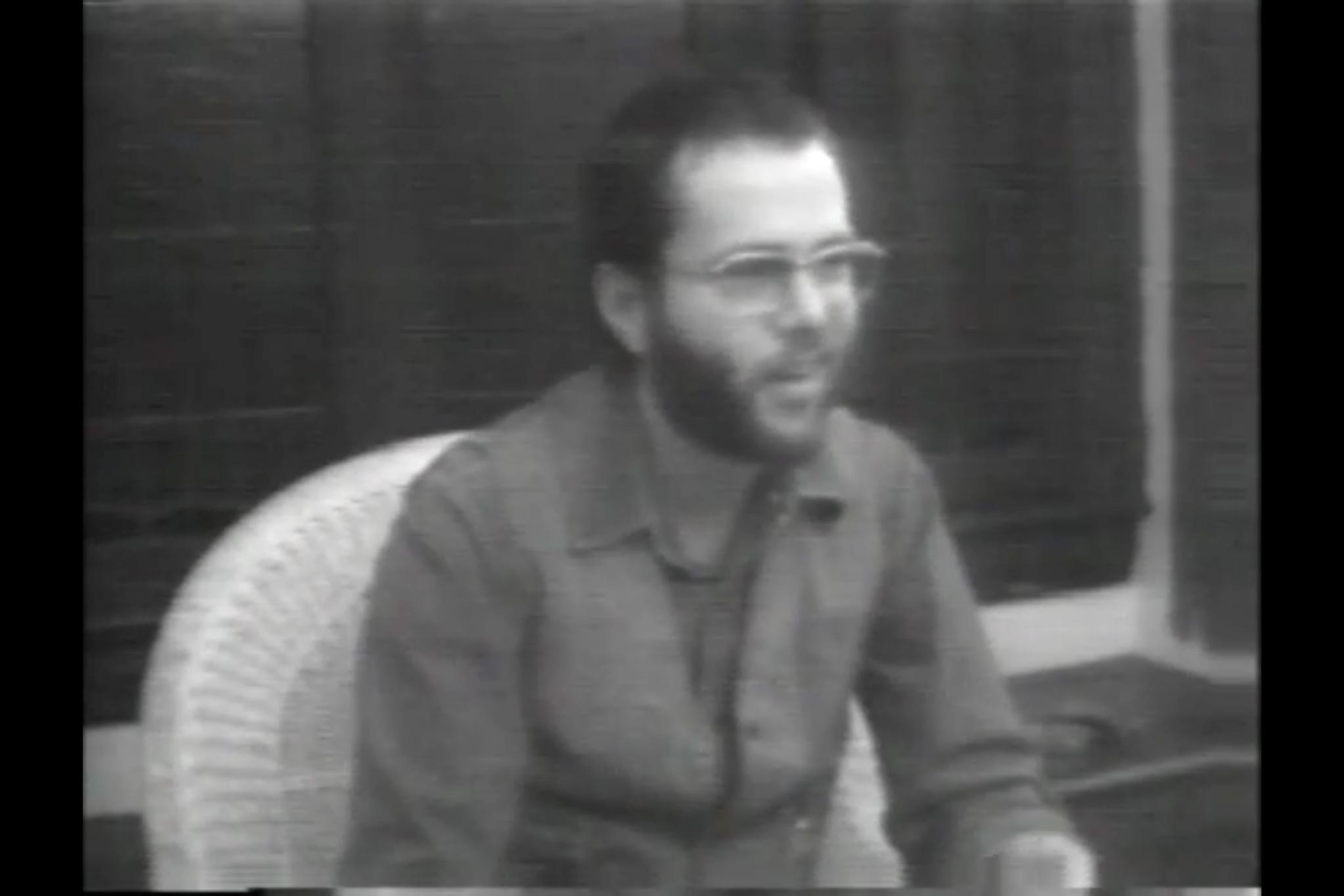 Black and white image of a man with a beard and glasses talking looking to the right.